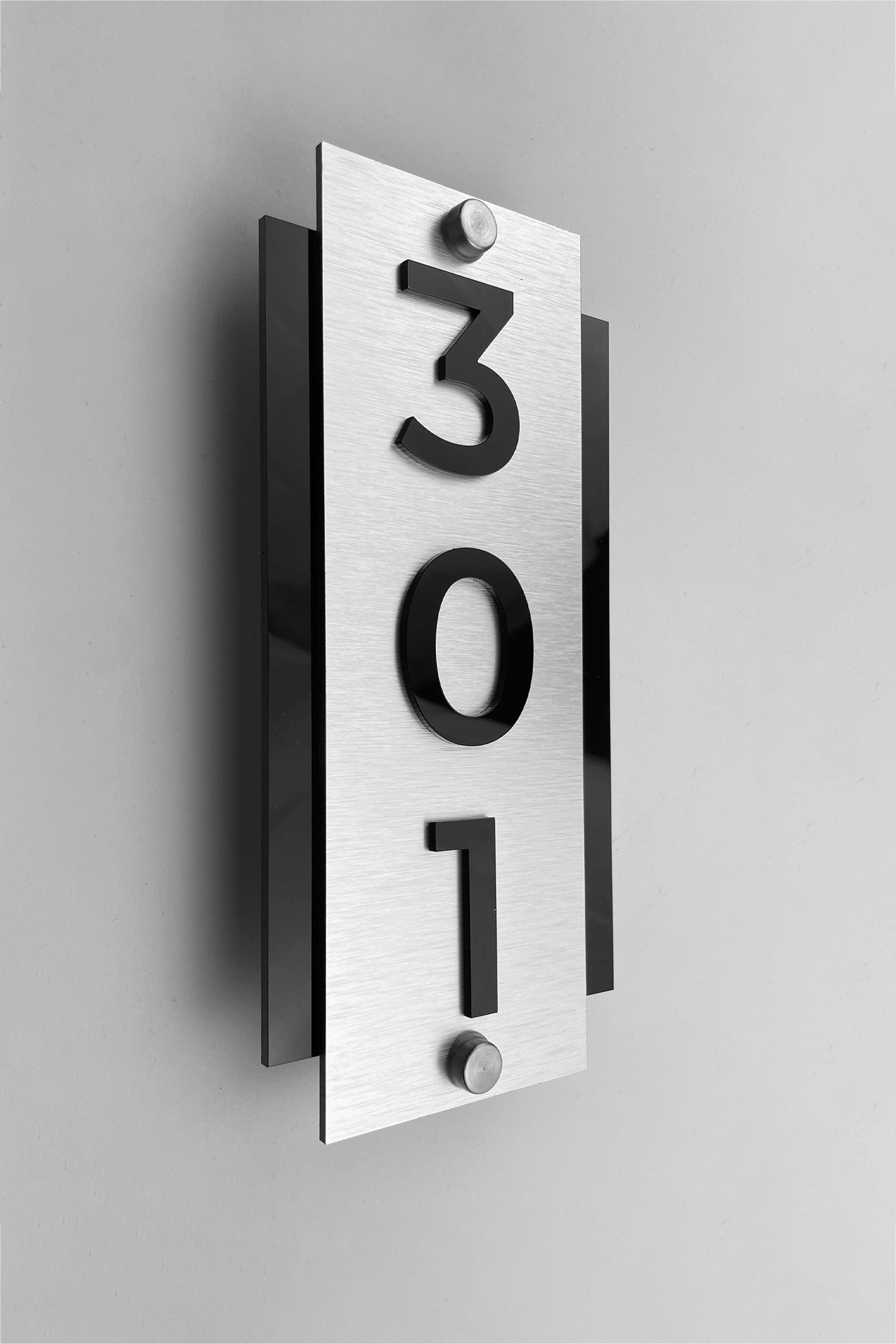 Vertical hotel room number sign by ALUMADESIGNCO with silver metal plaque and raised acrylic numbers, modern standoff door signage for hotel corridors and apartments