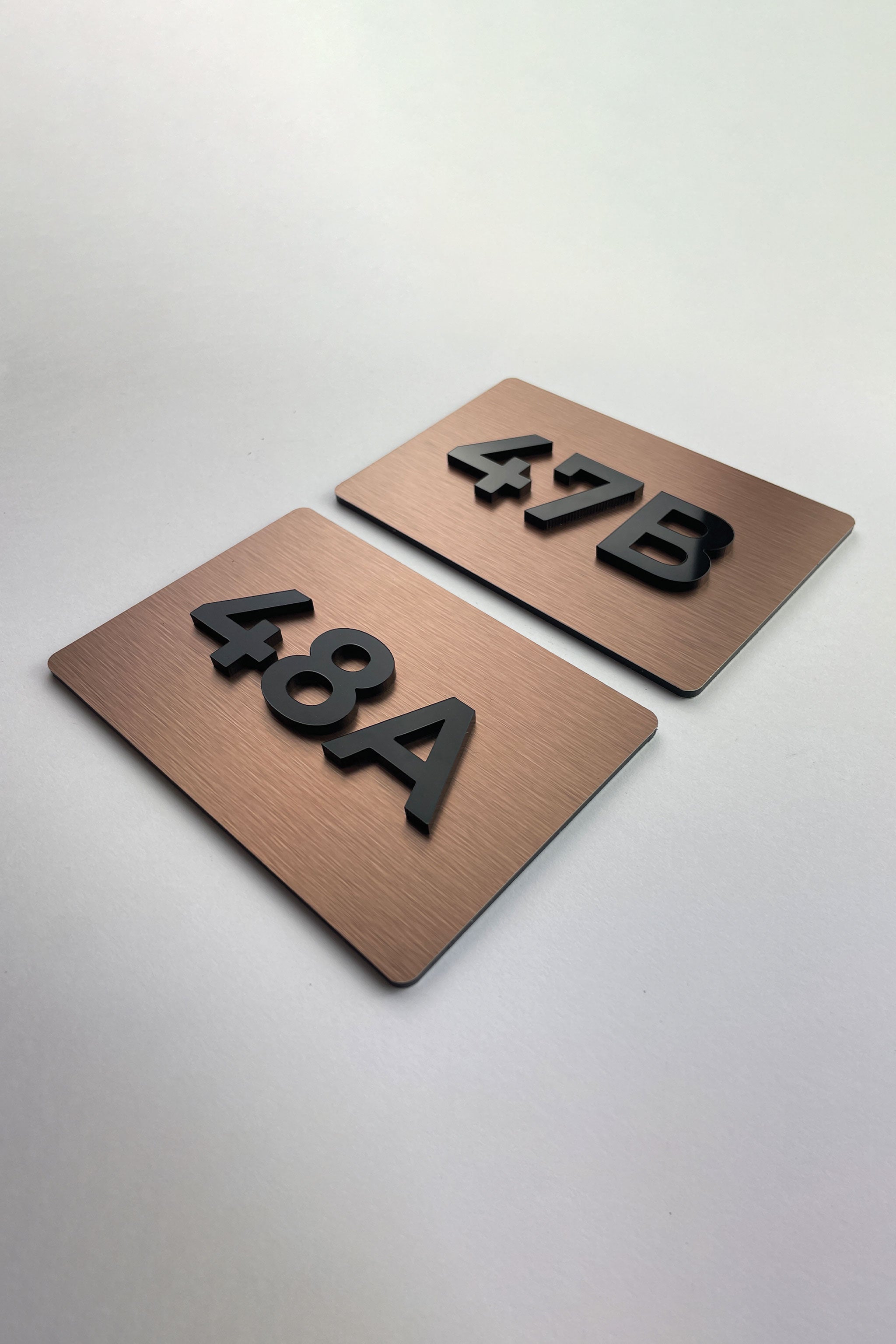 Brushed bronze door number sign by ALUMADESIGNCO featuring metal plaque and acrylic numbers, elegant signage for hotel rooms and apartment interiors