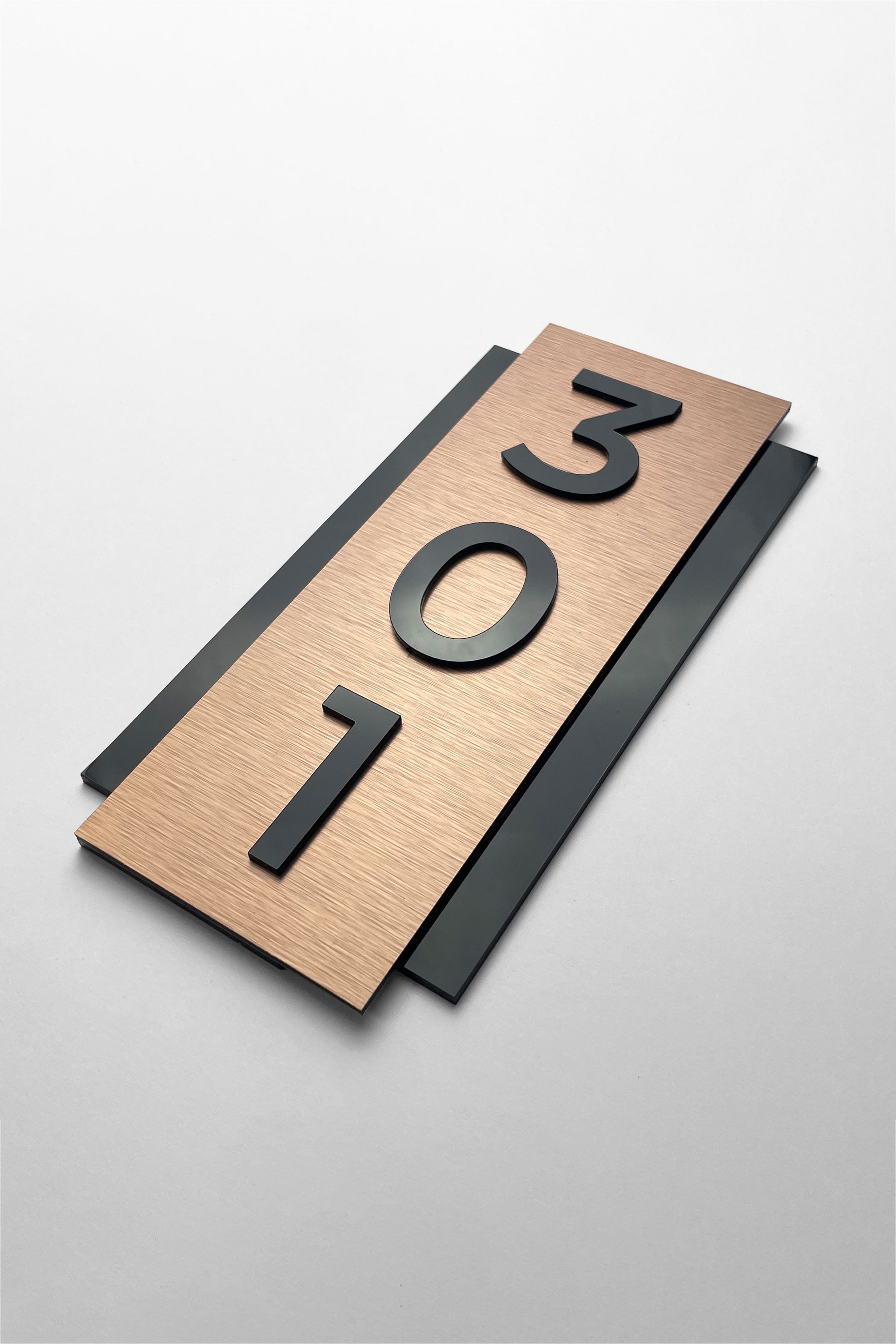 Vertical brushed bronze room number plaque by ALUMADESIGNCO featuring bronze aluminum panel and raised black acrylic glass numbers, modern hotel door signage for corridors and apartments