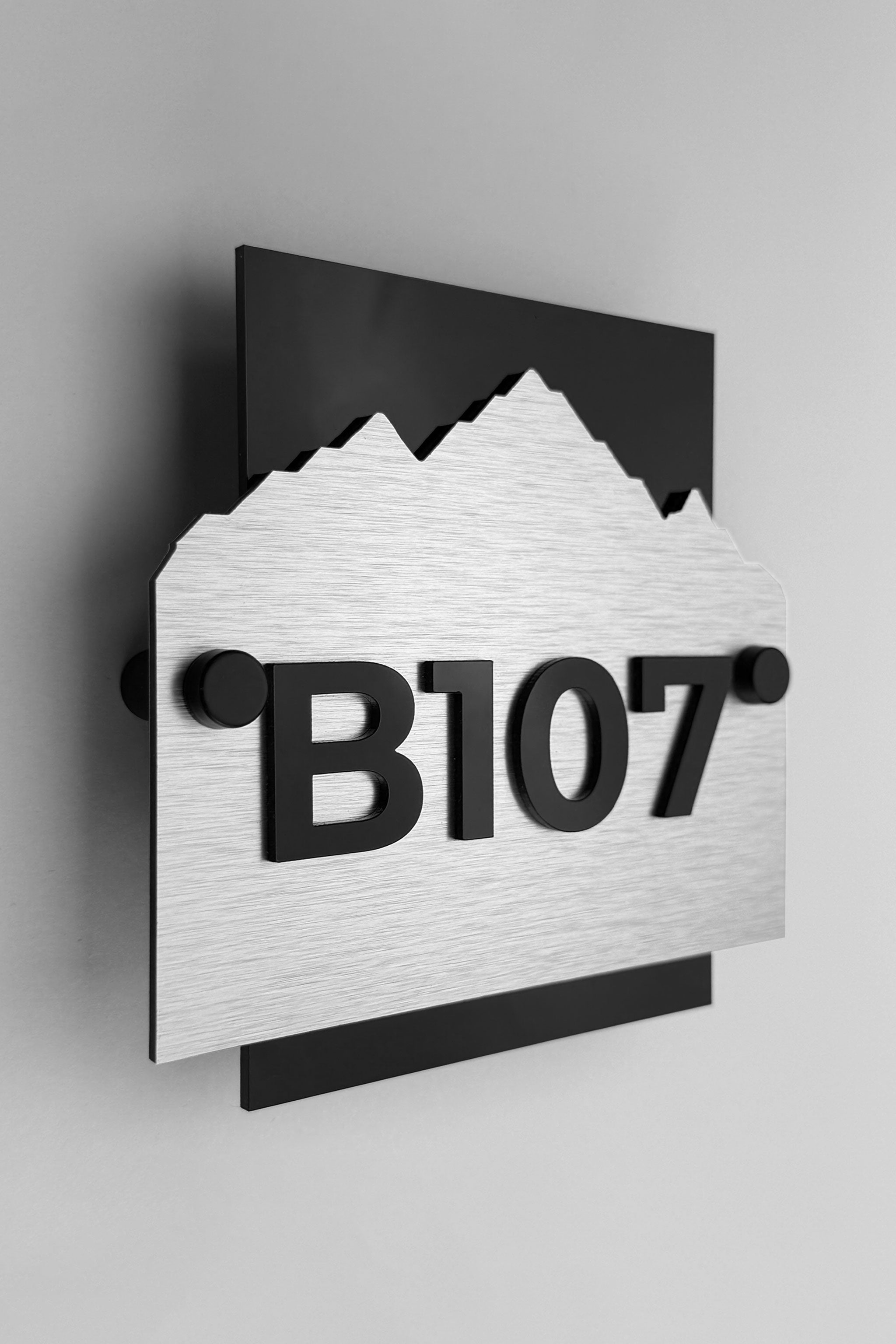 Custom Alpine hotel wall number sign by ALUMADESIGNCO featuring brushed silver metal plaque and black acrylic numbers, modern hotel room door signage for corridors and hospitality interiors