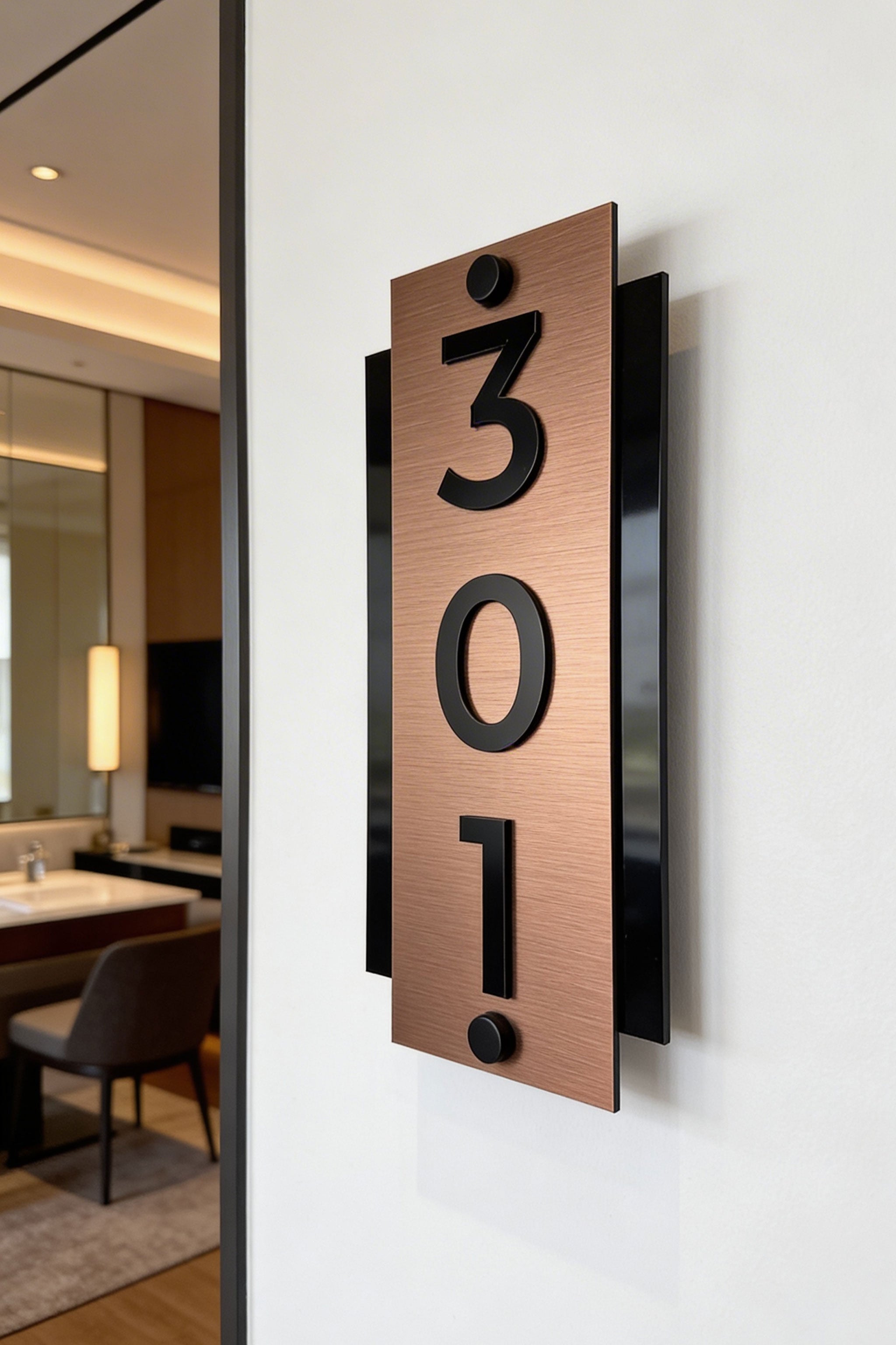 Modern vertical brushed bronze hotel door number sign by ALUMADESIGNCO combining bronze metal panel and raised acrylic numbers, elegant standoff wall signage