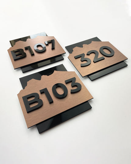 Modern Alpine Design hotel room number sign by ALUMADESIGNCO combining brushed bronze metal panel and acrylic numbers, stylish door signage for contemporary interiors