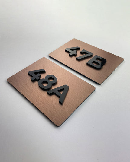 Brushed bronze door number sign by ALUMADESIGNCO featuring metal plaque and acrylic numbers, elegant signage for hotel rooms and apartment interiors