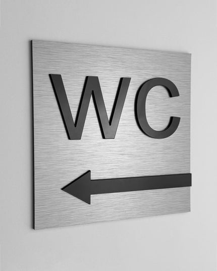 ALUMADESIGNCO WC sign with left arrow and minimalist modern style, restroom wayfinding signage for offices, hotels, cafés, and contemporary interiors