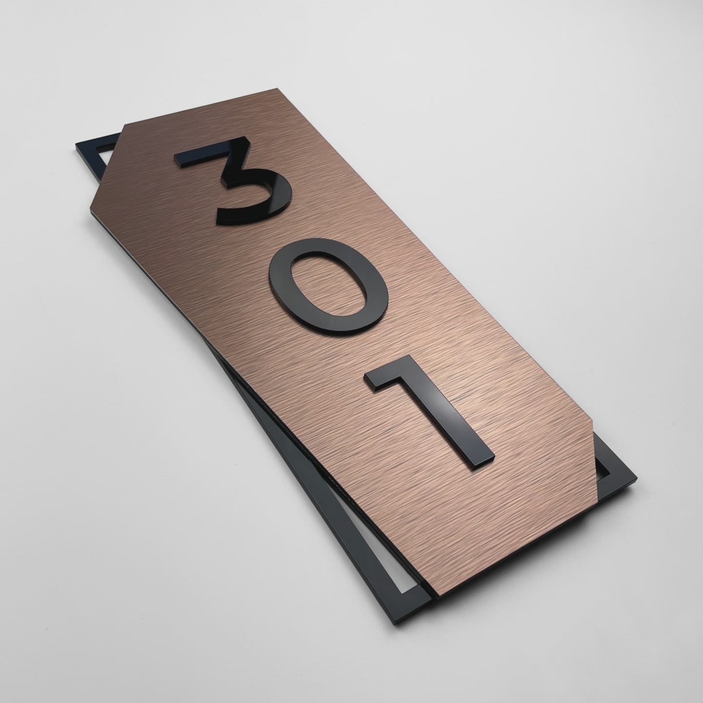 Modern vertical brushed bronze hotel room number plaque by ALUMADESIGNCO combining bronze aluminum panel and raised black acrylic numbers, elegant signage for hotel interiors